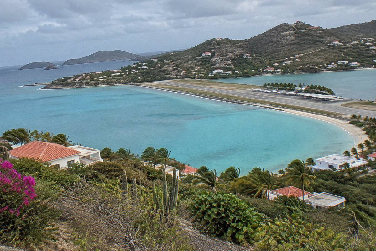 Aerial view of a turquoise bay with a thin strip of runway and small aircraft parked beside palm trees