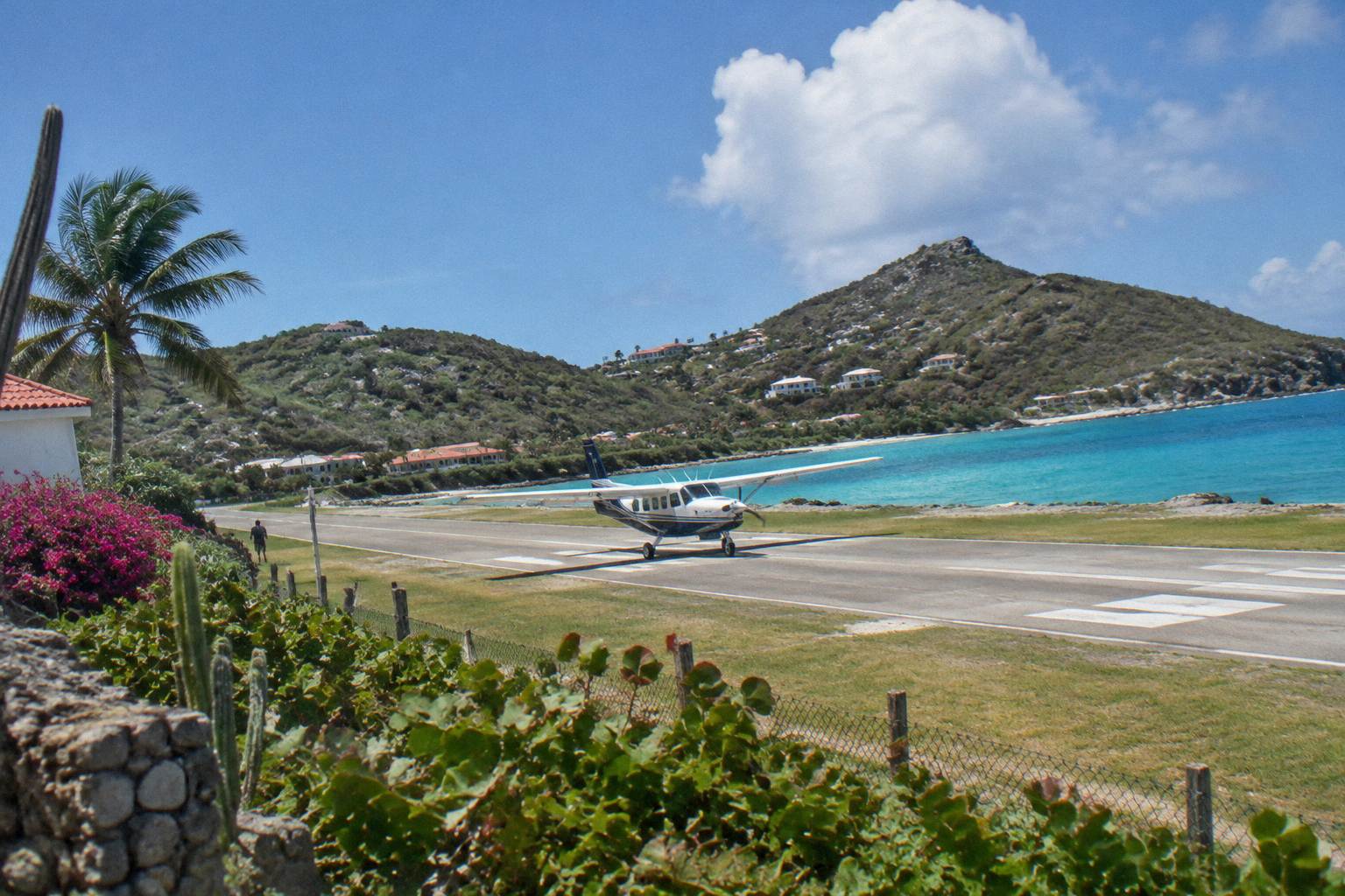 A small propeller aircraft on a short Caribbean runway with green hills behind it