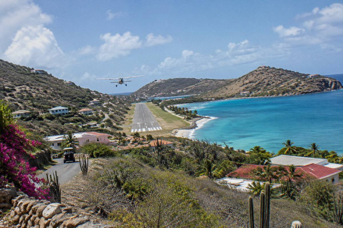 A small aircraft descending toward a short Caribbean runway beside a turquoise bay