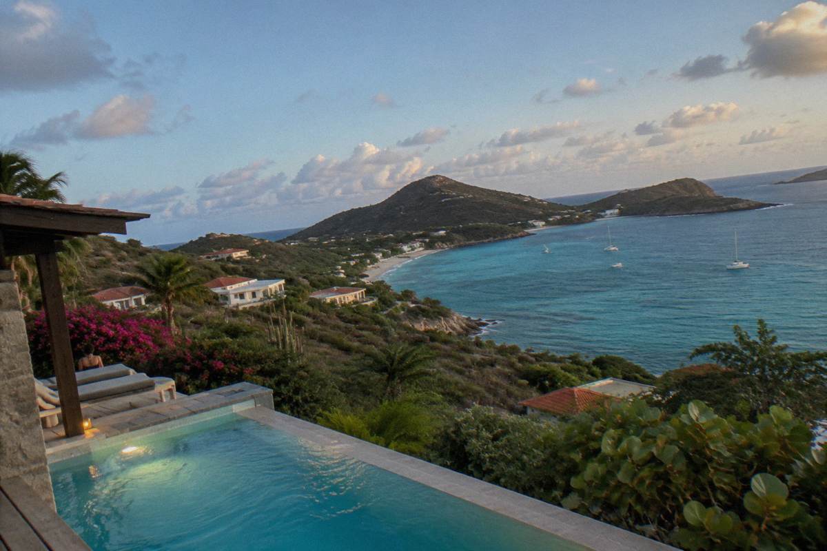 A dark hillside villa terrace with a lit pool overlooking a dim coastline