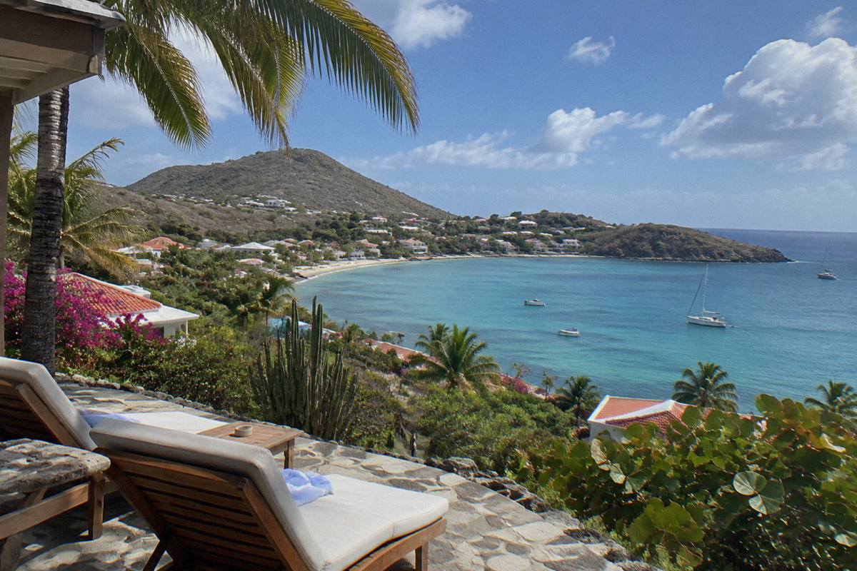 Small hotel terrace overlooking a calm bay with sun loungers and palm shade