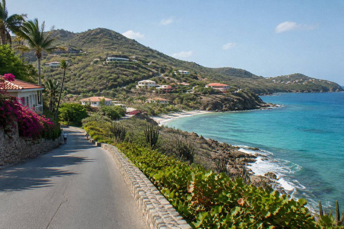 Coastal road curving between green hills and a rocky shoreline in late afternoon light