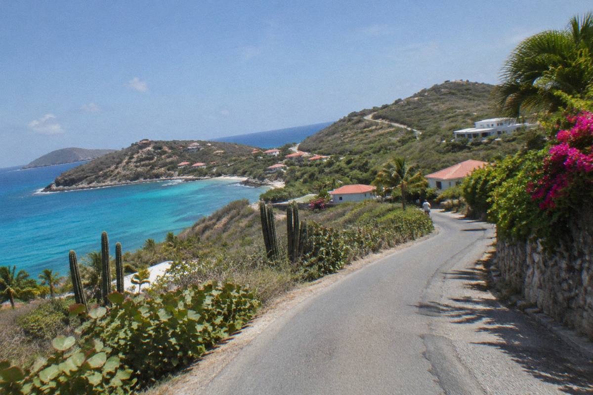 A narrow island road curving between low green hills with no other cars visible