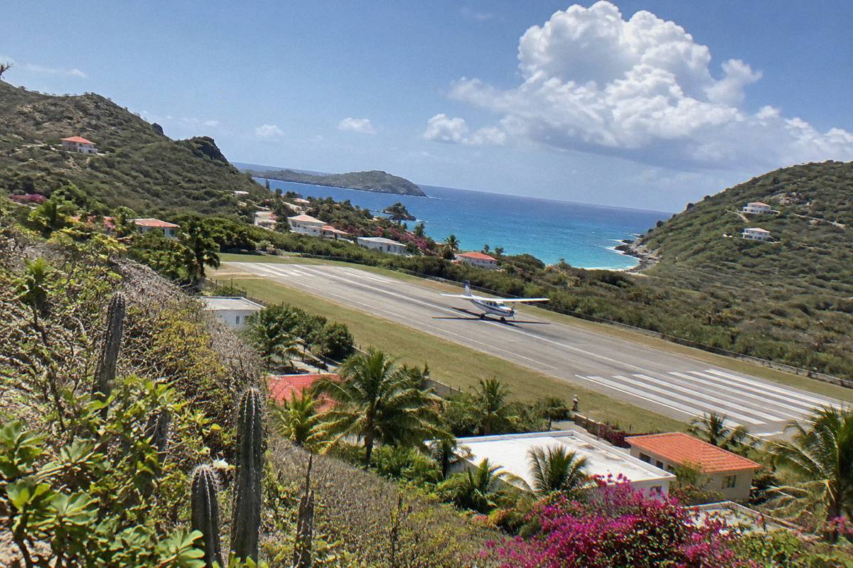 Small aircraft on a short runway between green hills near the sea