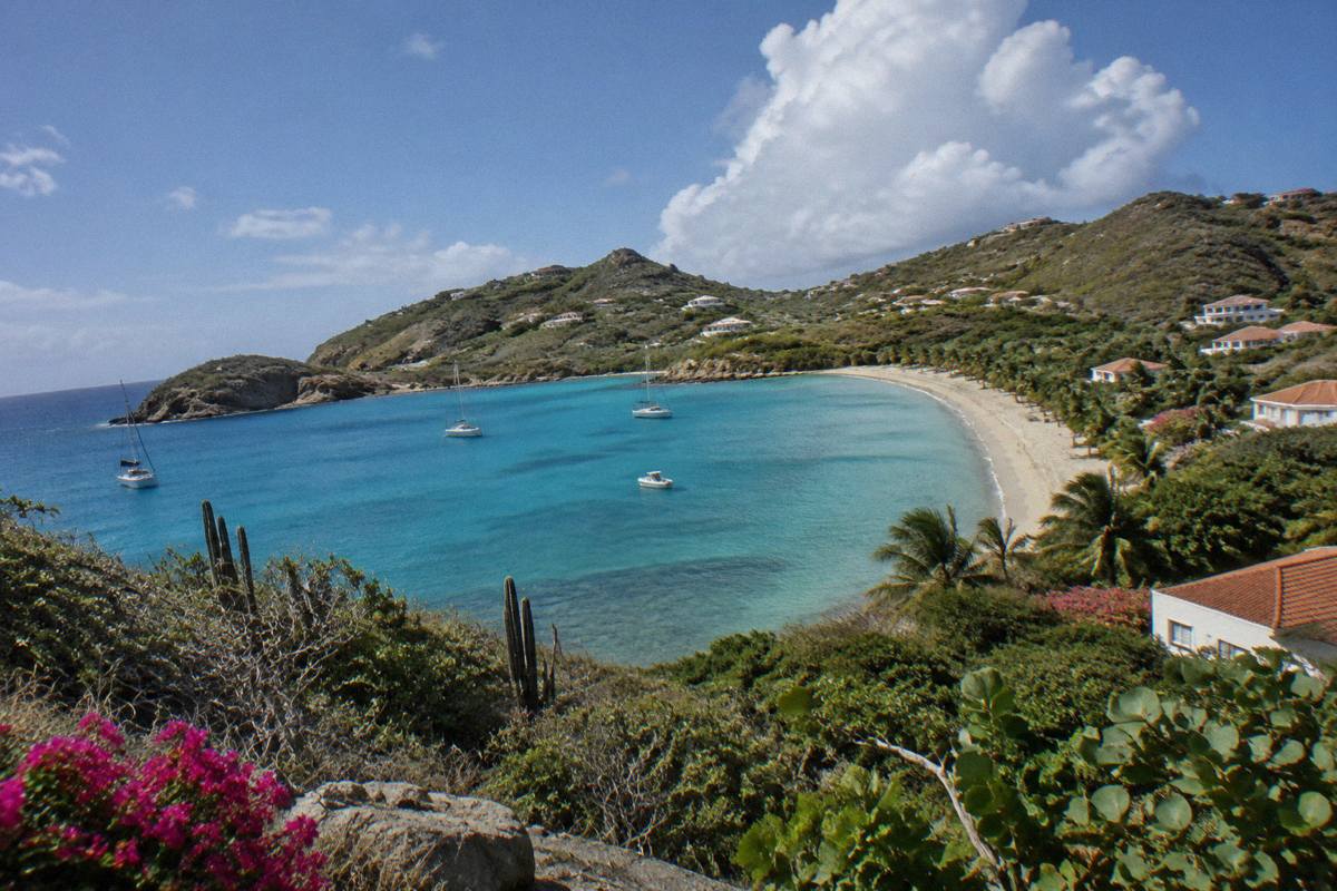 A calm Caribbean bay with turquoise water and a curve of sand fringed by low green hills