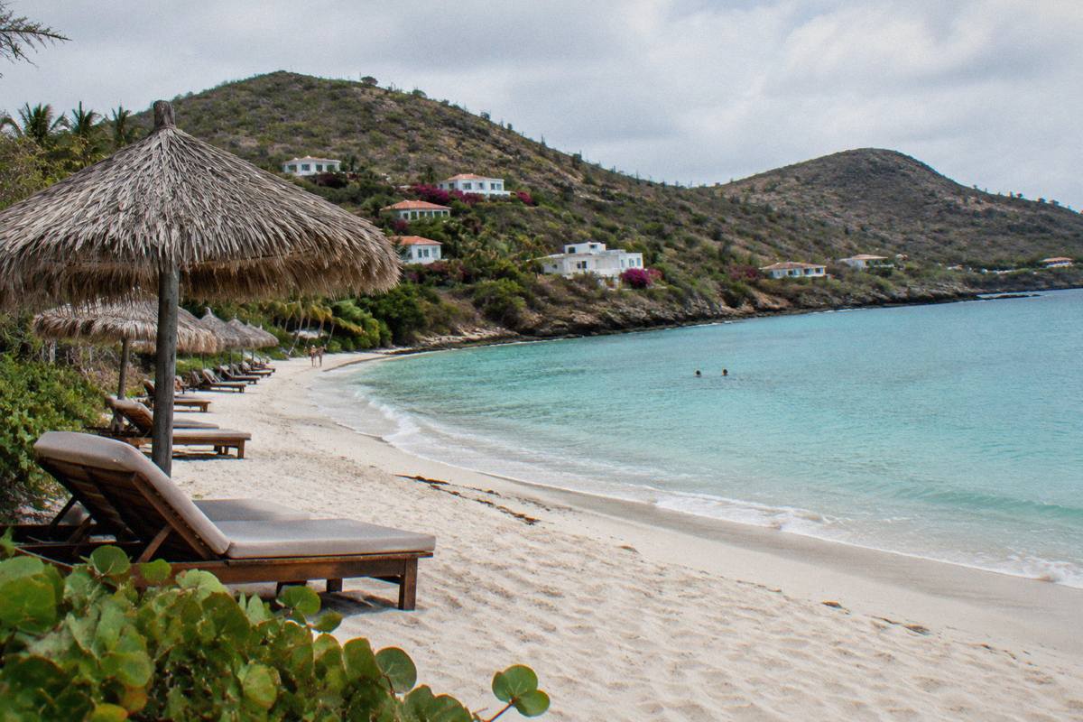 Wooden sun loungers and thatched umbrellas on white sand beside calm turquoise water