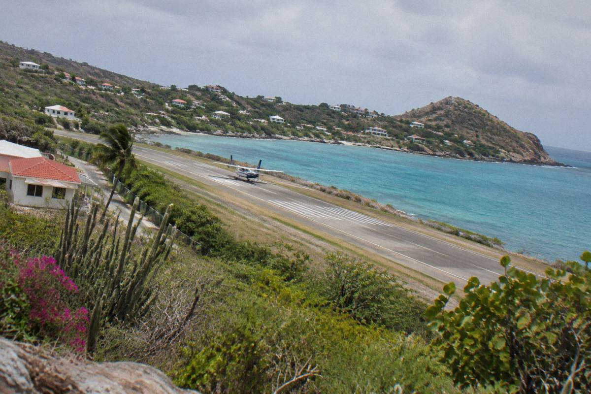 A small aircraft on a short runway between a hillside and a turquoise bay.
