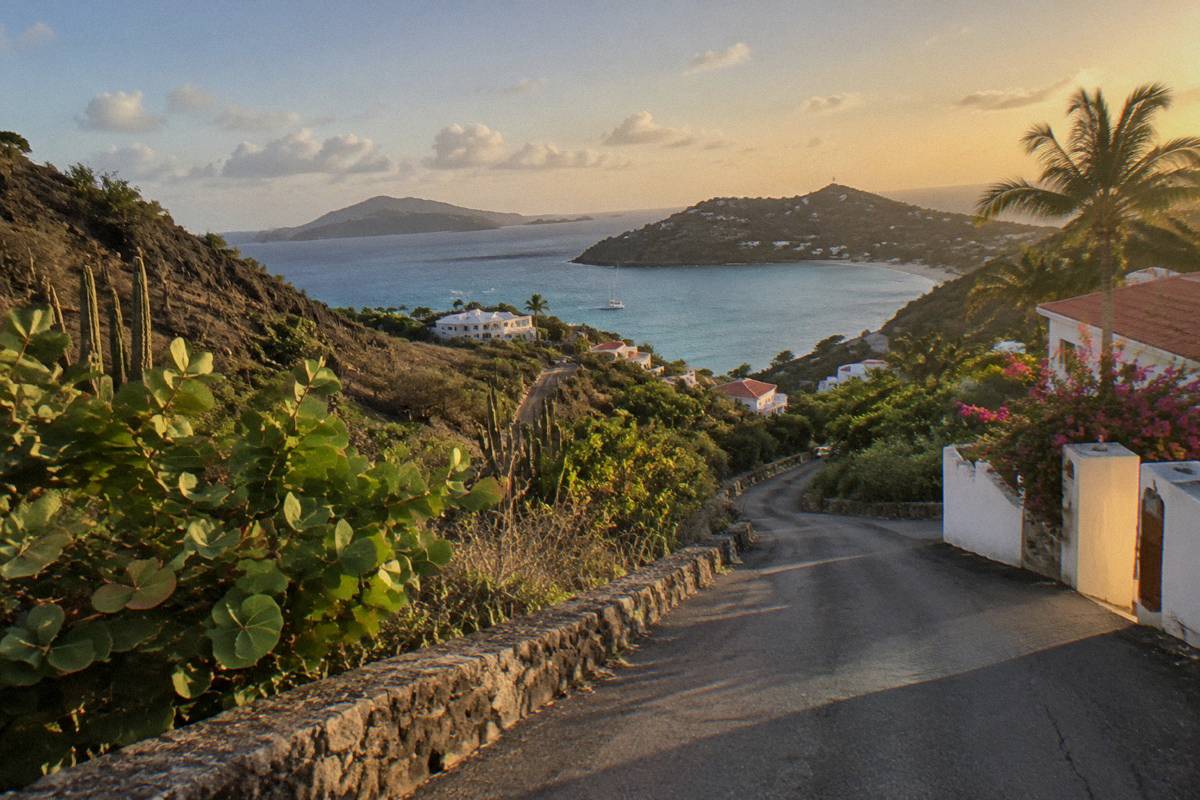 An empty island road winding between green hills toward a distant bay