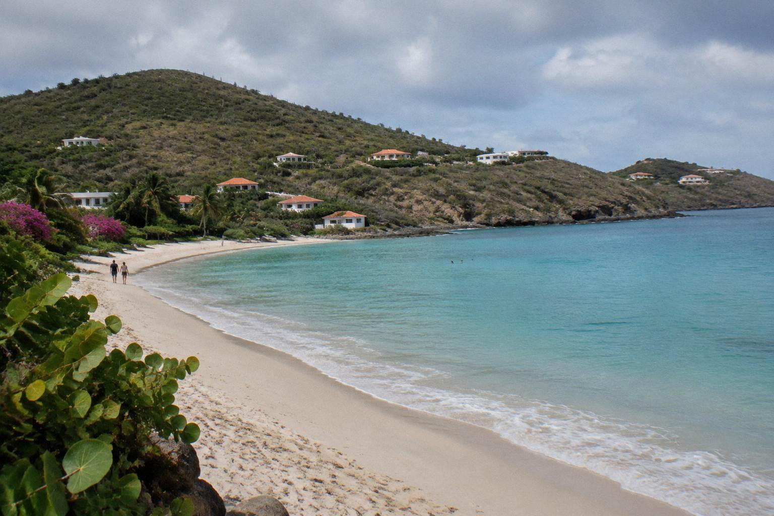 Wide sandy beach at Flamands with calm turquoise water and green hillsides