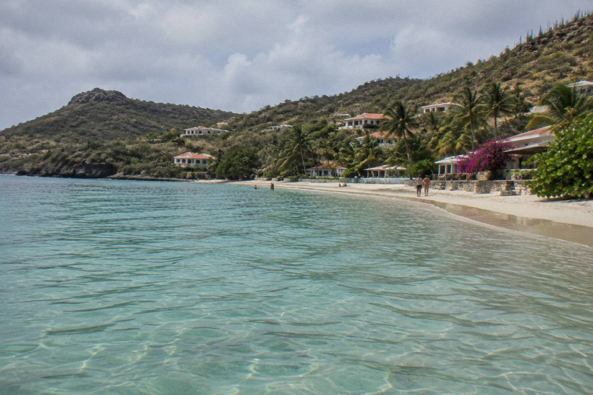 Shallow clear water of Grand Cul-de-Sac bay with palm trees and a low hotel terrace along the sand