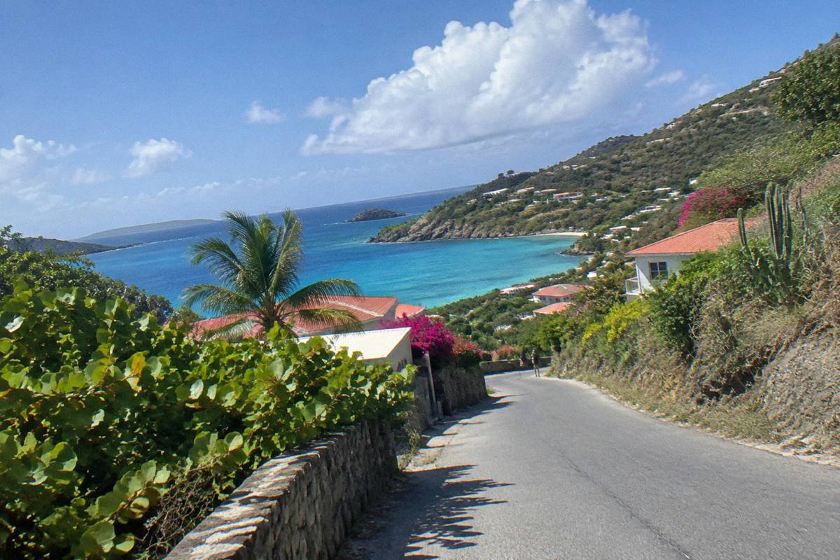 Narrow island road curving between green hillsides with glimpses of blue sea beyond
