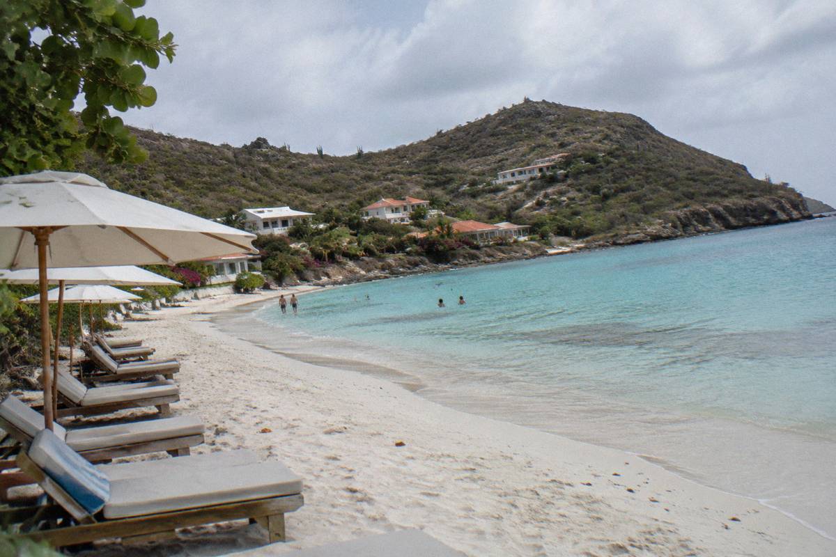 Row of beach loungers and umbrellas on white sand beside calm shallow water