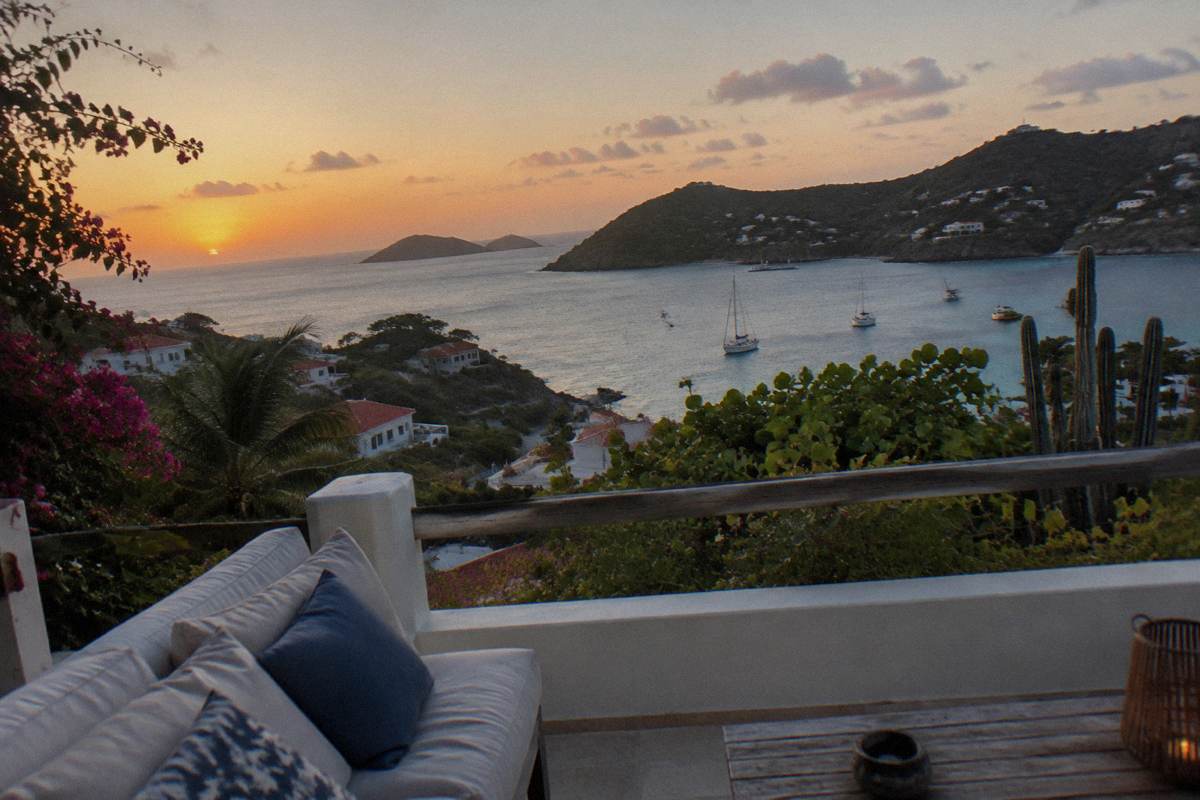 A terrace of a Caribbean rental house at dusk with cushions and a view over darkening water