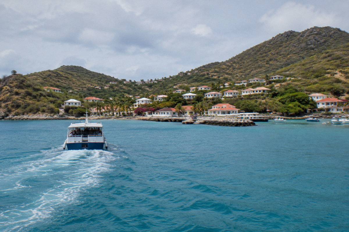 A passenger ferry crossing open blue water toward a small harbour town on a green island