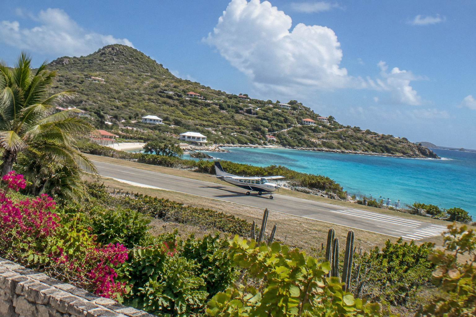 A small aircraft on a short Caribbean runway with green hills rising behind it