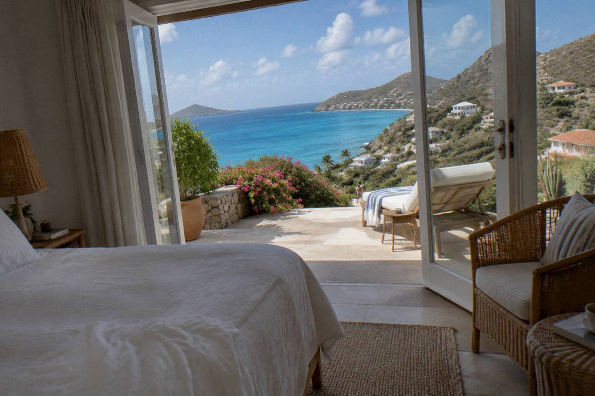 An elegant hotel suite interior with white linens, rattan furniture and open doors to a terrace
