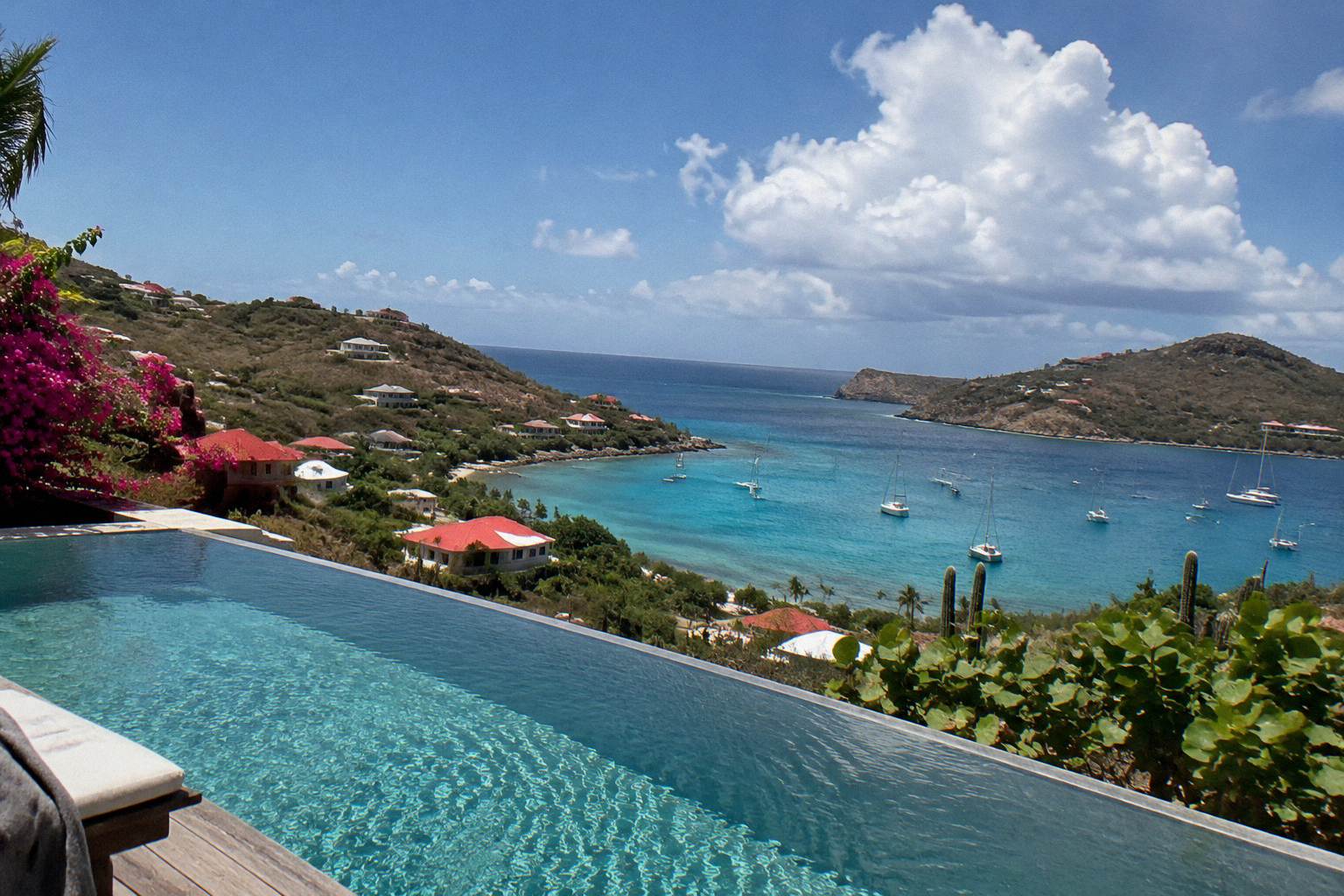 A quiet infinity pool terrace overlooking a Caribbean bay at dusk with sailboats anchored offshore