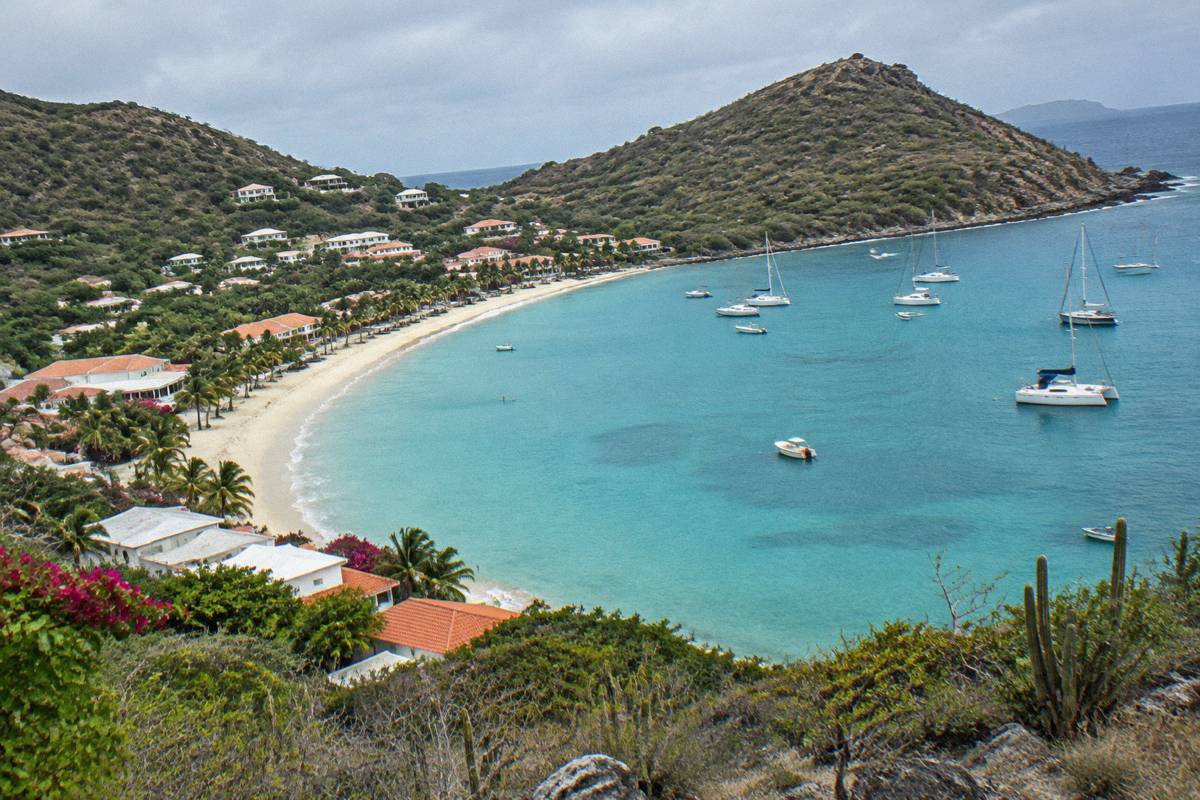 Aerial view of a curved bay with resort buildings along the sand and moored boats