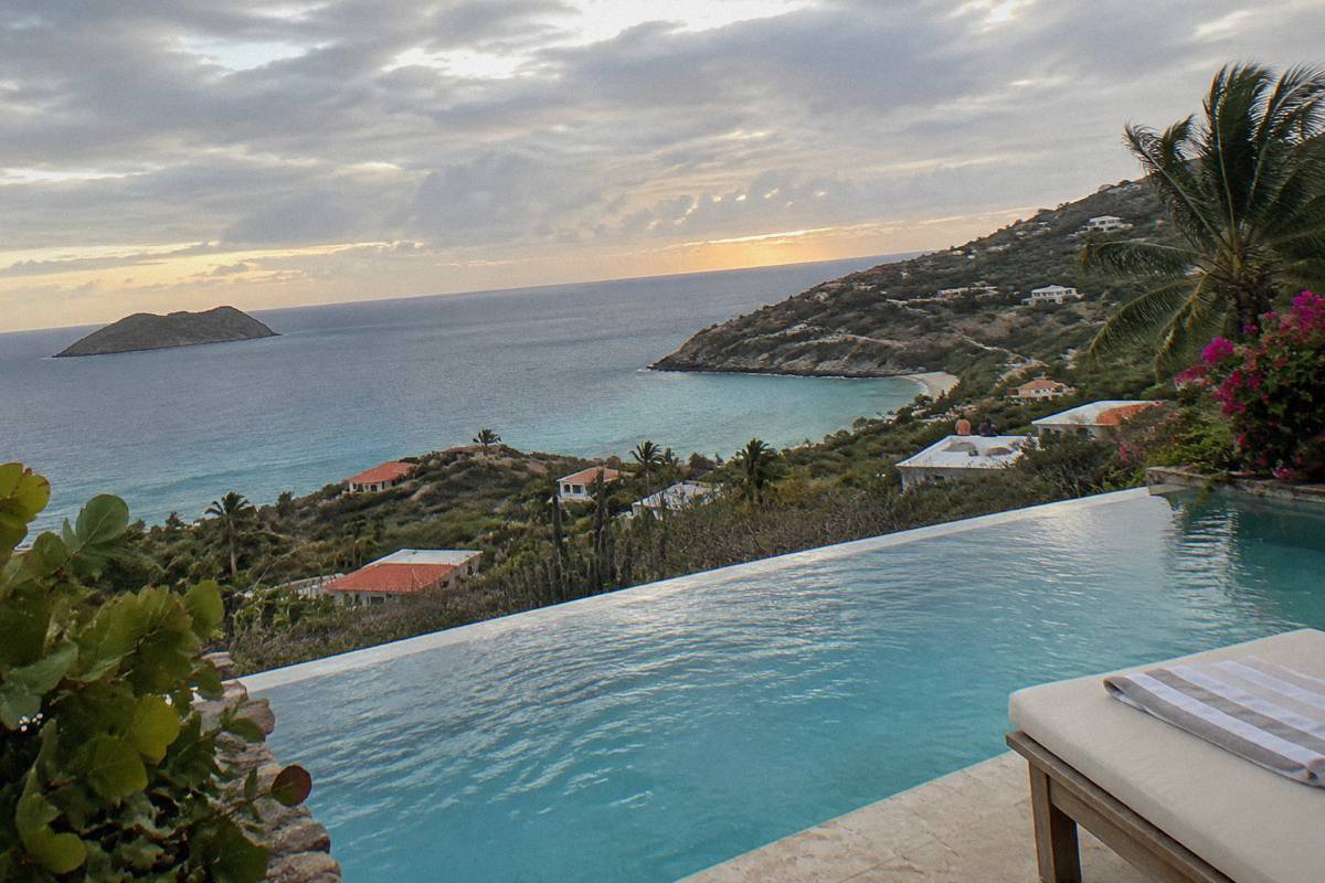 An infinity pool edge at sunset with the sea horizon beyond and a lounge chair at the side