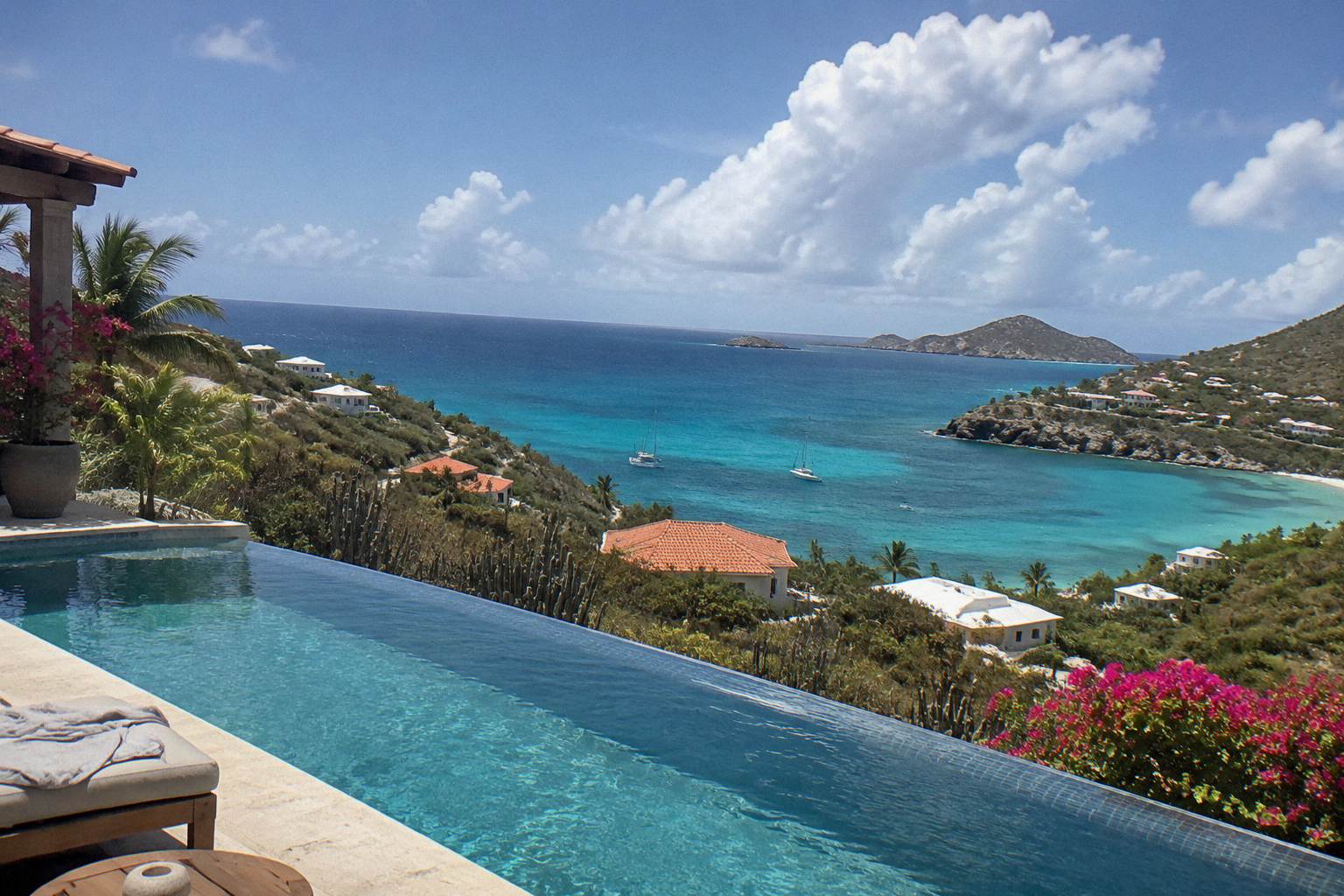 A hillside villa terrace with an infinity pool overlooking the Caribbean sea at dusk