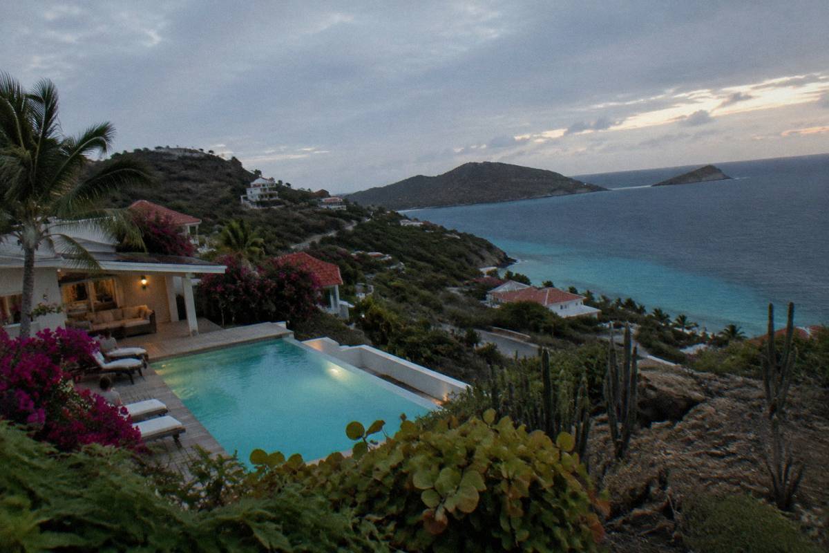 A hillside villa with a lit pool terrace looking over dark water at dusk