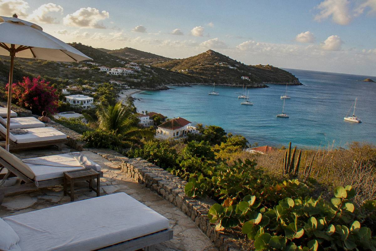 A hotel terrace with white loungers facing a calm bay in warm evening light