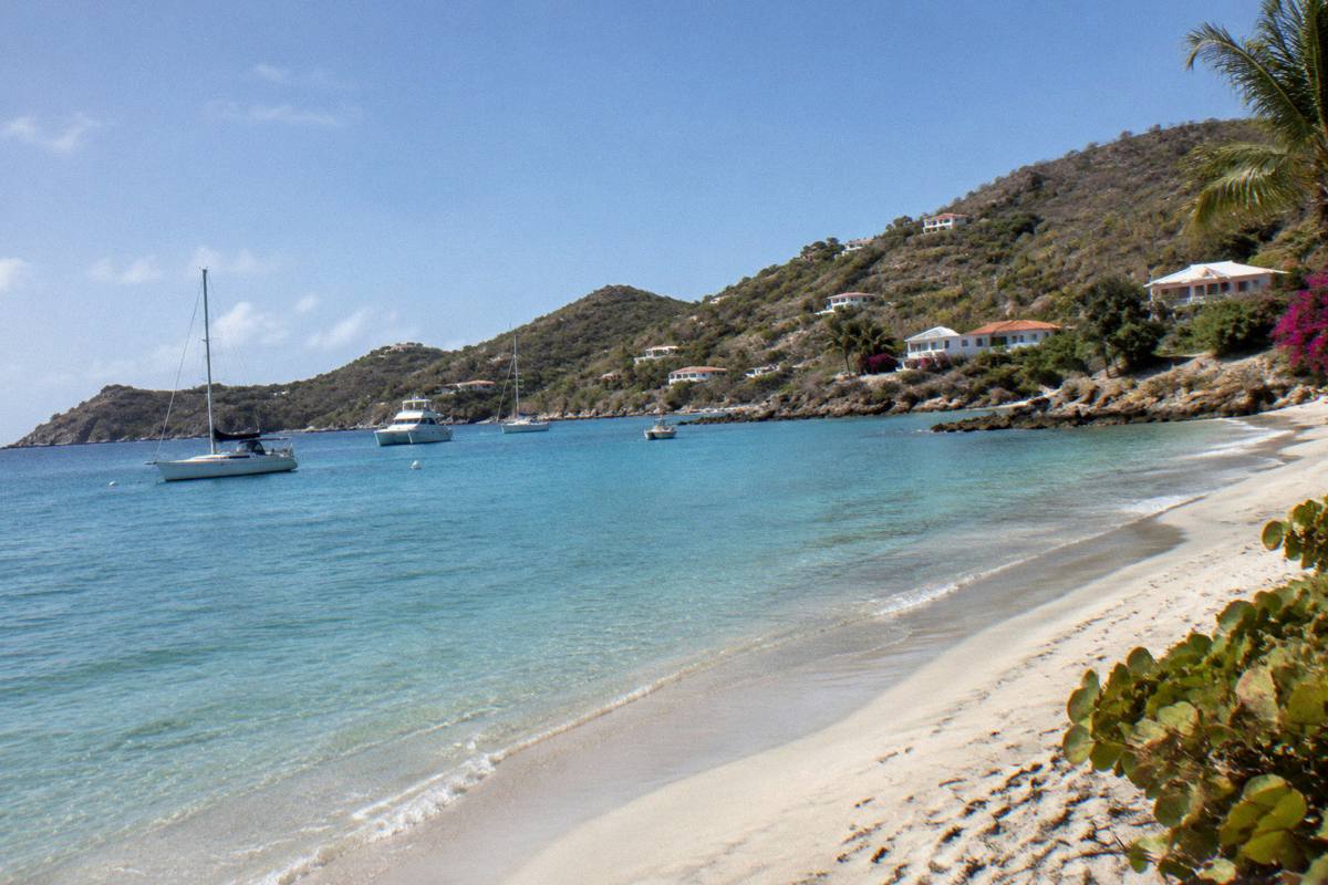 An empty beach with calm water and a few boats at anchor under a clear morning sky