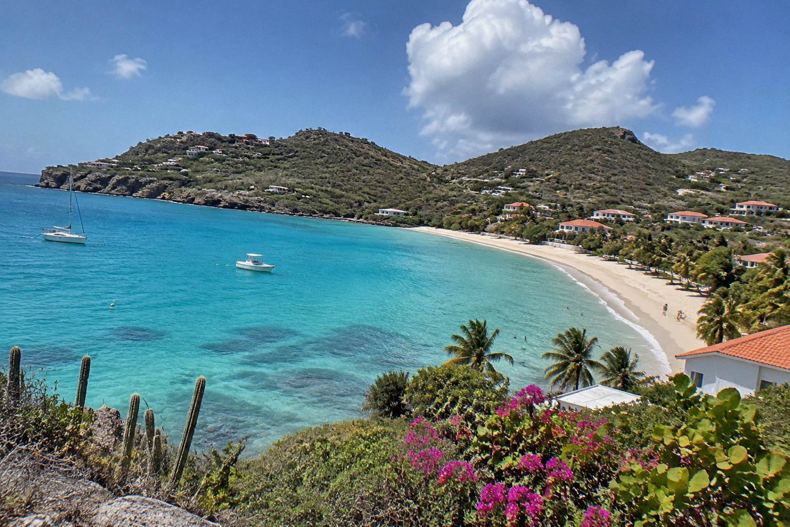 A calm turquoise bay on Saint Barthelemy with a curved sandy shore and green hills behind