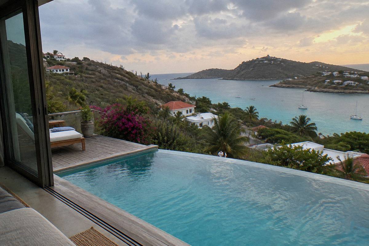 A private villa infinity pool at dusk with an open sliding door