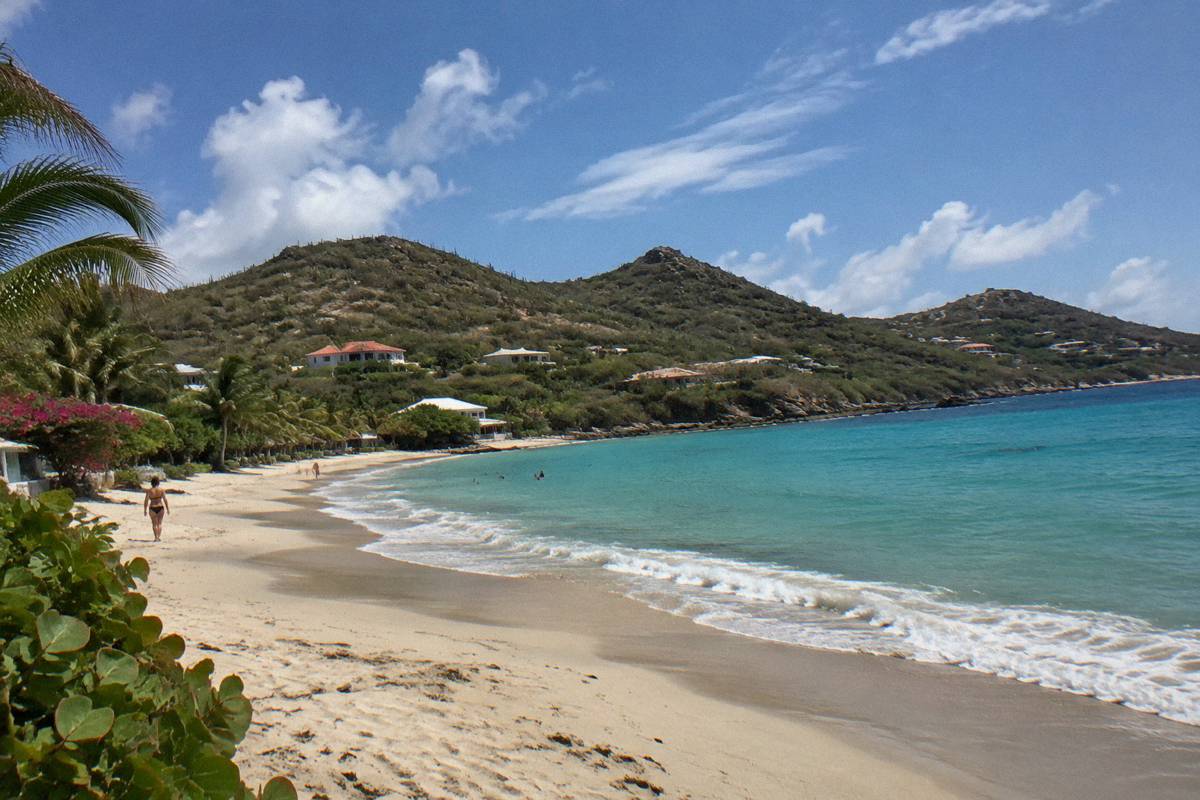 A wide sandy beach with gentle waves and low green hills behind