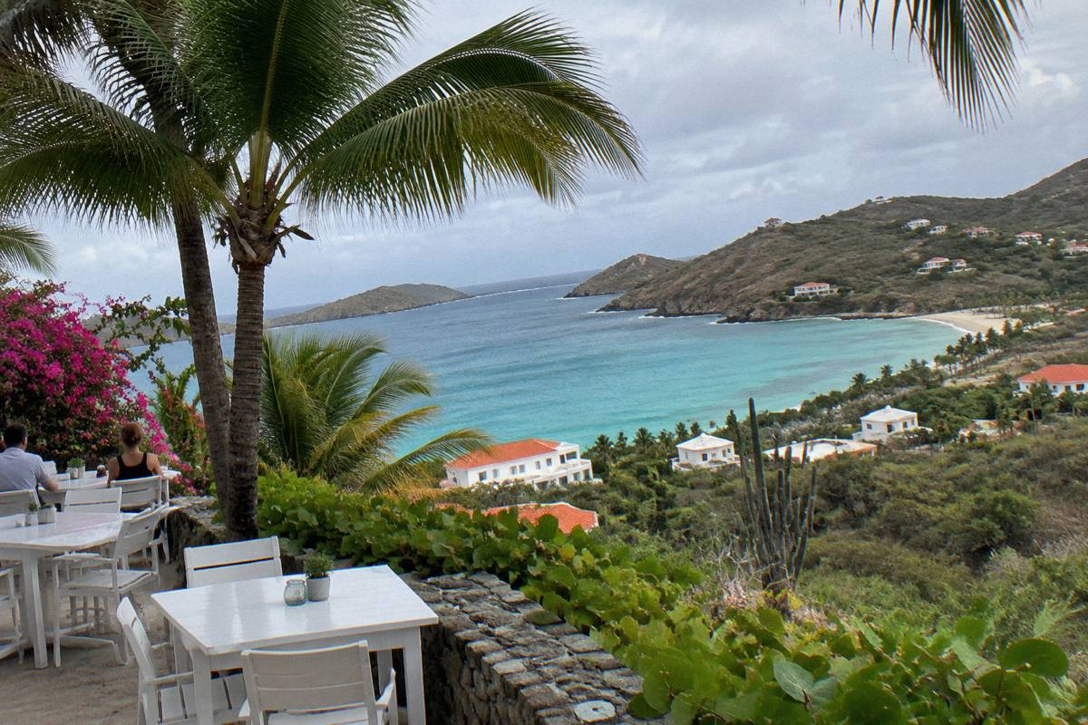 Small hotel terrace with white tables under palm trees near the water