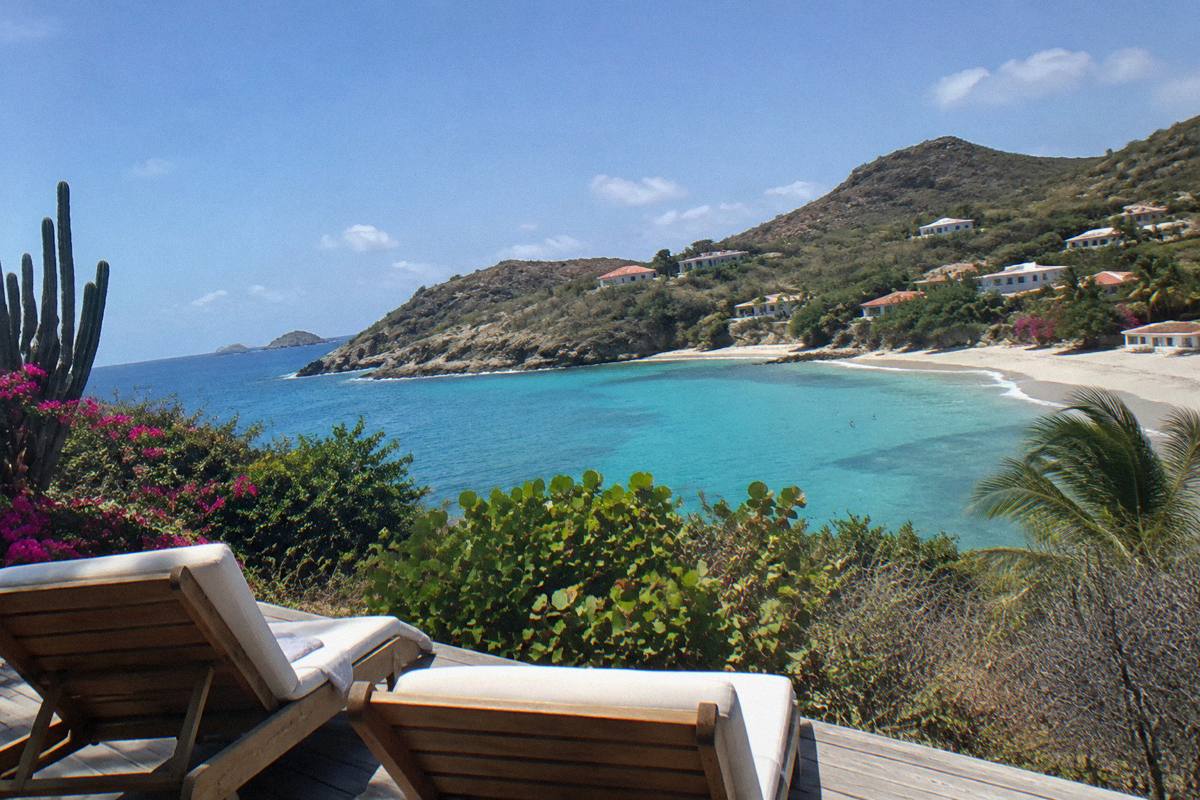 Wooden deck chairs and an open shoreline under a wide sky at midday