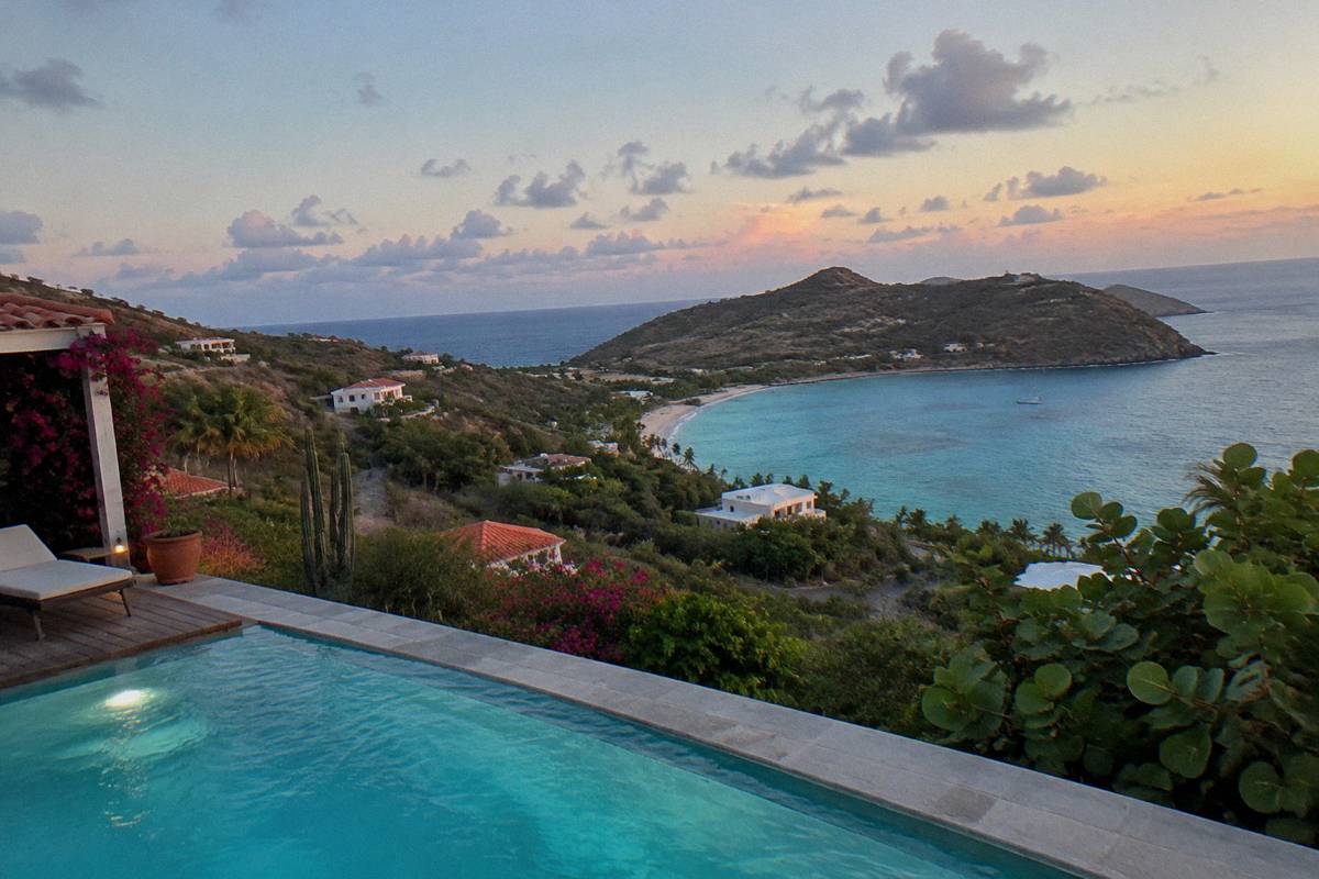 Lit pool at a villa terrace after dusk with sea horizon