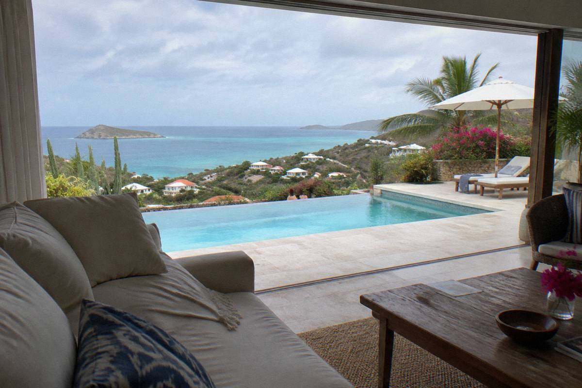 Sunlit villa living room opening onto a pool deck with sea horizon beyond