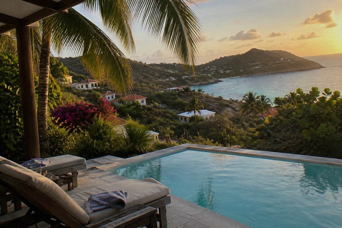 Shaded villa pool terrace with sun loungers and palm fronds above turquoise water