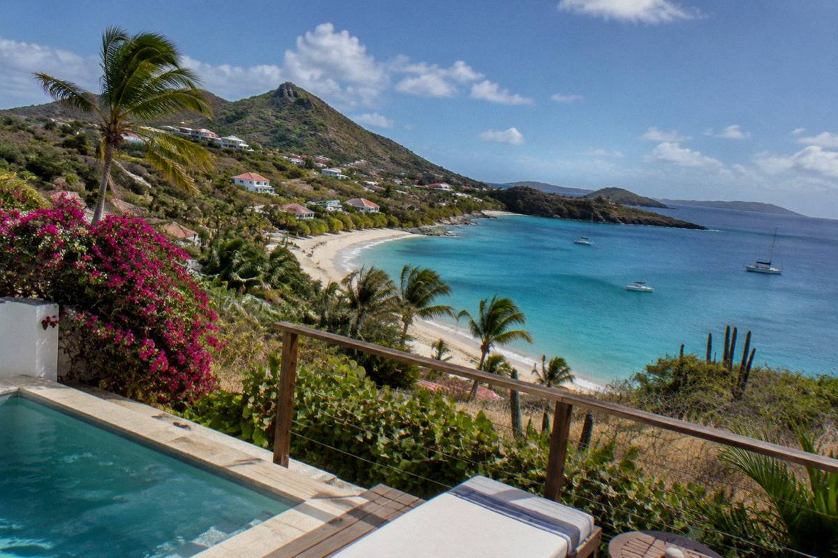Villa terrace above a palm-lined beach with calm water and green hills in the distance