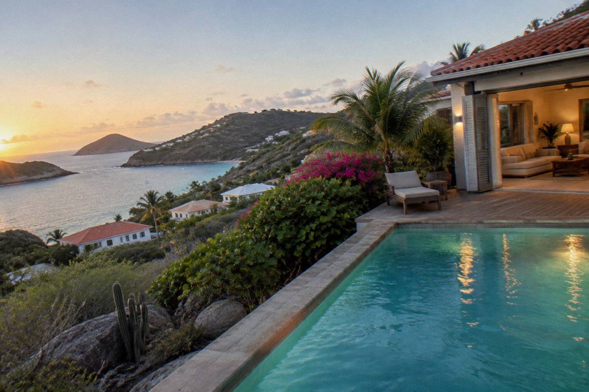 Evening view of a lit private pool and villa interior seen through open glass doors