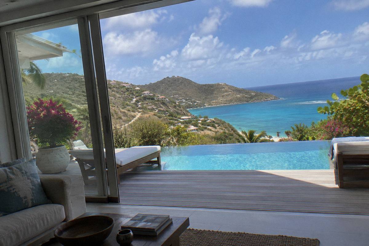 Modern villa interior opening through glass doors onto a pool deck and sea view