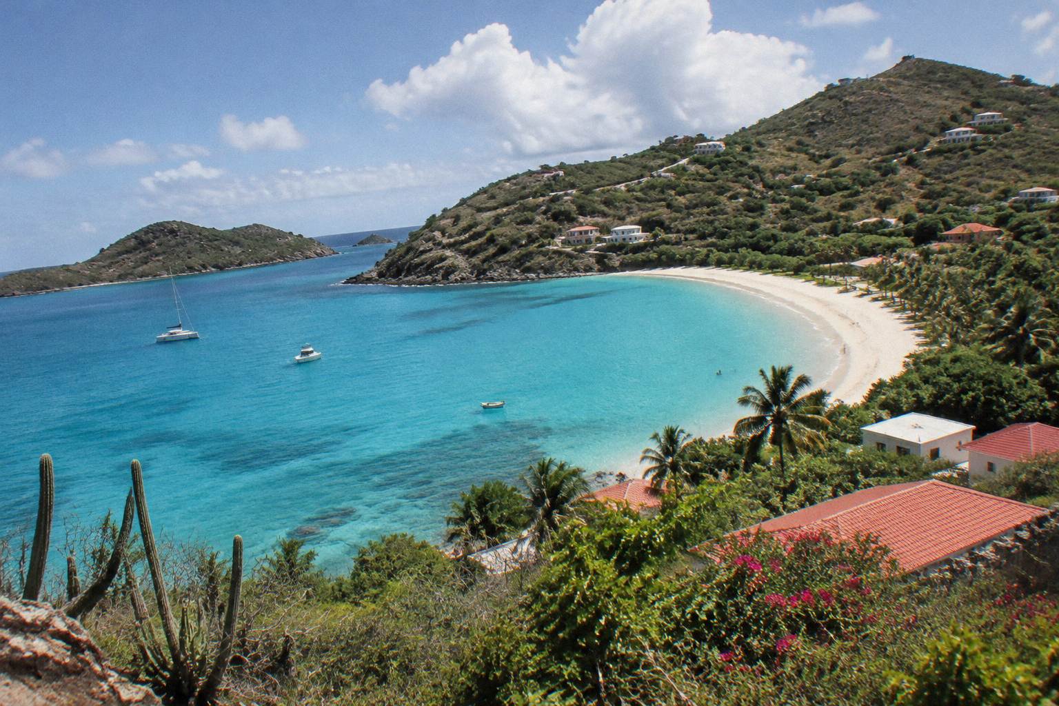 Turquoise bay with white sand beach and green hillsides dotted with low buildings
